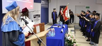 Inauguracja na UTH w Płońsku, studenci składają przysięgę w akademickich togach i z flagą.