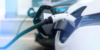 Elektryczny samochód podłączony do ładowania, z widocznym kablem wtyczkowym w gnieździe.