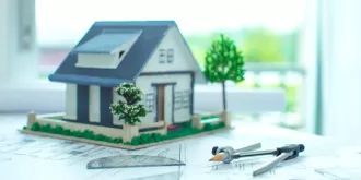 Model zielonego budynku z planami architektonicznymi oraz narzędziami do rysowania na stole.
