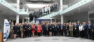 Grupa uczestników konferencji stoi na schodach w Akademii Marynarki Wojennej, uśmiechając się do kamery.