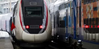 Pociągi stają obok siebie na stacji, tworząc dynamiczną scenę kolejową w nowoczesnym otoczeniu.