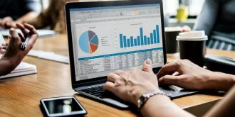 Osoba pracuje na laptopie, analizując dane z wykresami i tabelami w kontekście big data podczas spotkania.