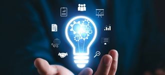 Dłonie trzymające świecącą żarówkę otoczoną cyfrowymi ikonami reprezentującymi innowacje i technologię