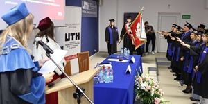 Inauguracja na UTH w Płońsku, studenci składają przysięgę w akademickich togach i z flagą.