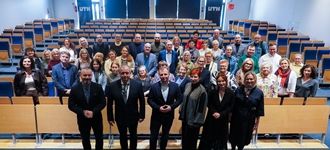 Uczestnicy konferencji oświatowej w UTH stoją razem w sali wykładowej, uśmiechając się do zdjęcia.