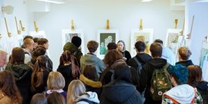 Grupa studentów ogląda wystawę sztuki, słuchając prelekcji prowadzonej przez artystkę.