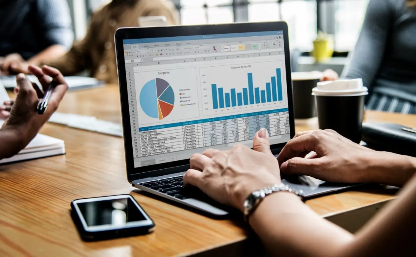 Osoba pracuje na laptopie, analizując dane z wykresami i tabelami w kontekście big data podczas spotkania.