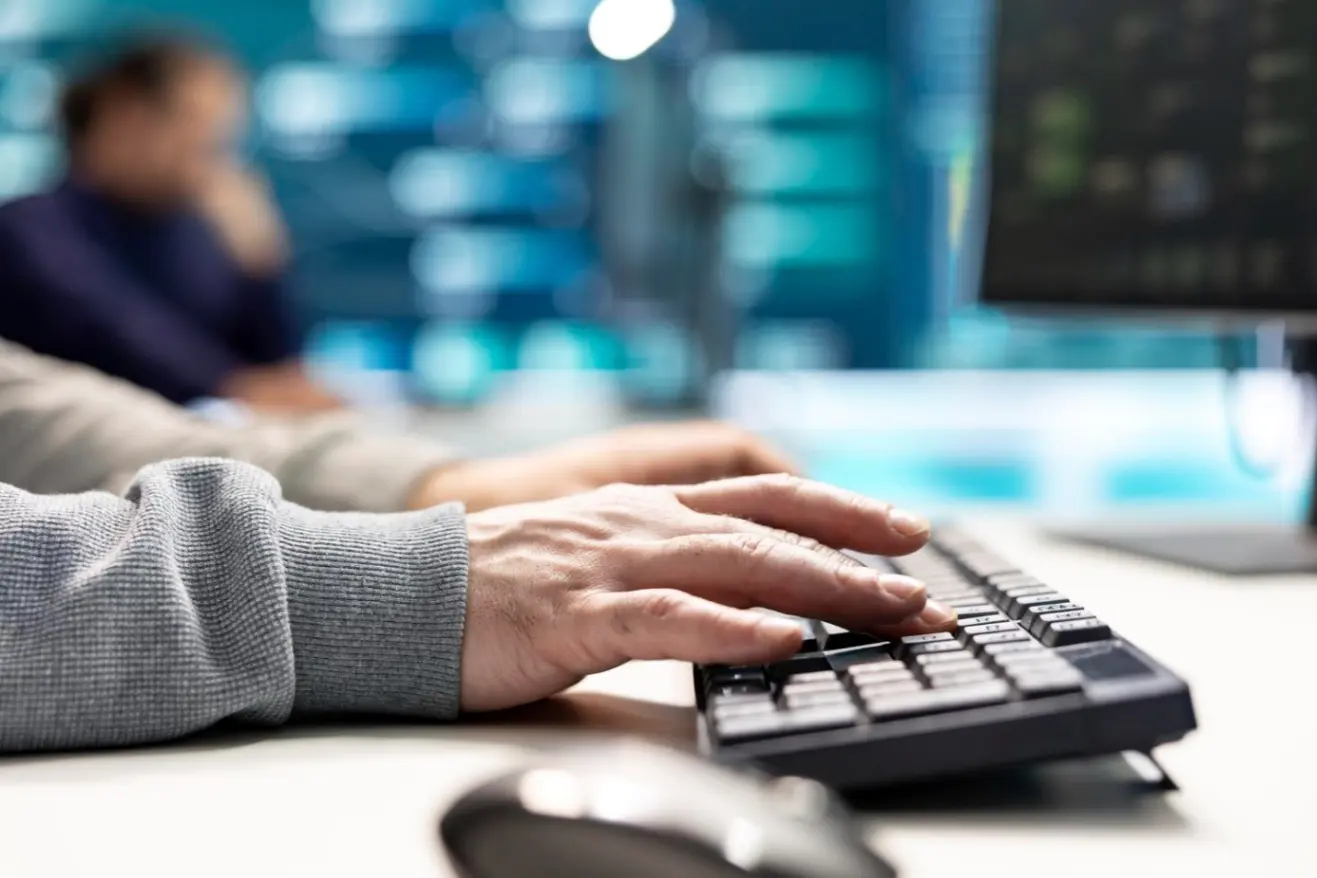 Osoba pracująca przy komputerze, mogąca analizować dane związane z cyberatakiem, z blaskiem ekranu w tle.