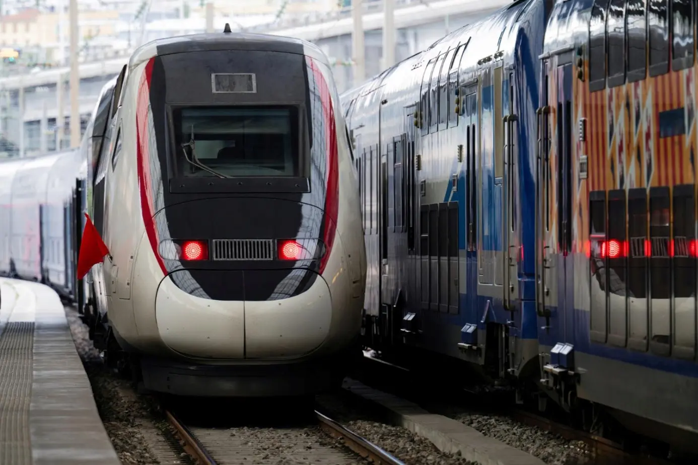 Pociągi stają obok siebie na stacji, tworząc dynamiczną scenę kolejową w nowoczesnym otoczeniu.