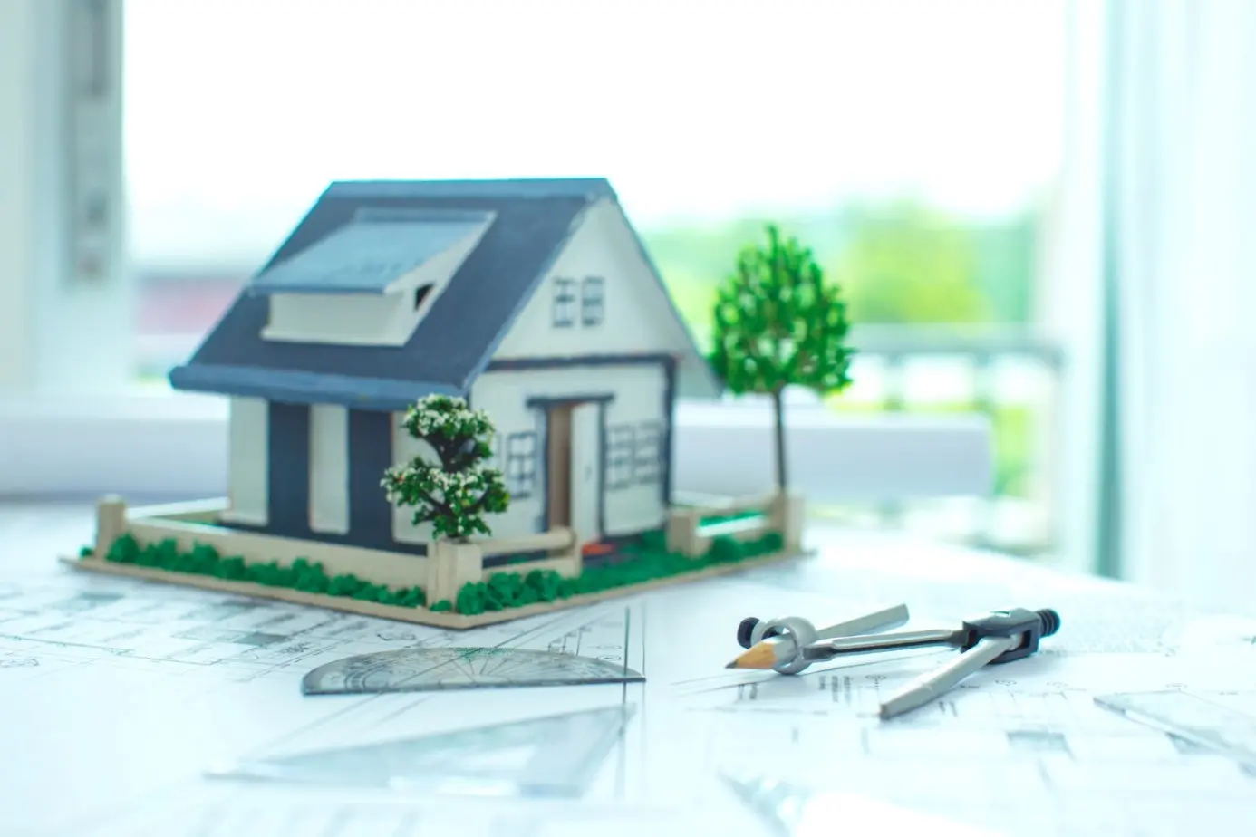 Model zielonego budynku z planami architektonicznymi oraz narzędziami do rysowania na stole.