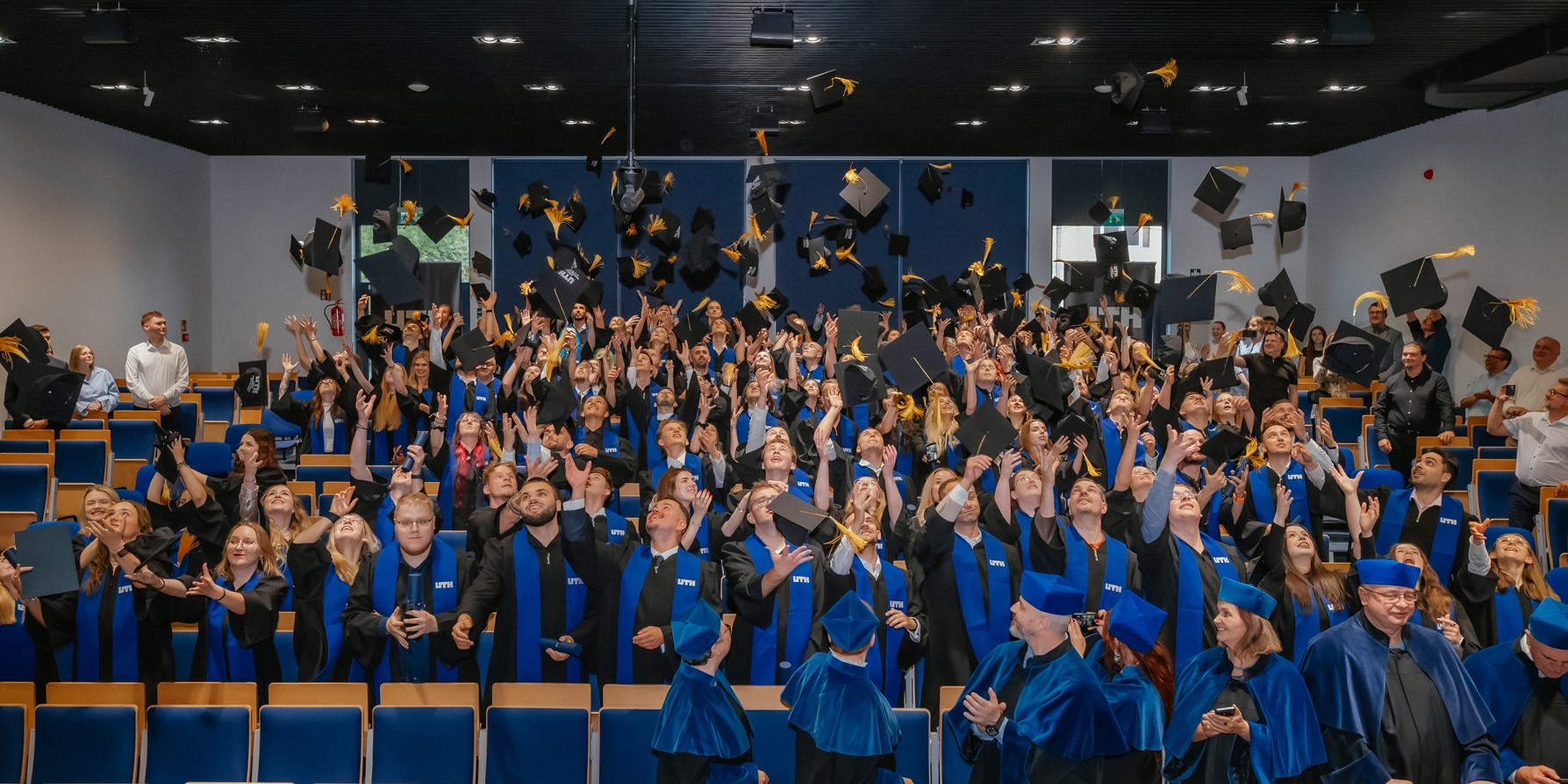 Studenci na ceremonii zakończenia studiów rzucają birety w powietrze w radosnej atmosferze.