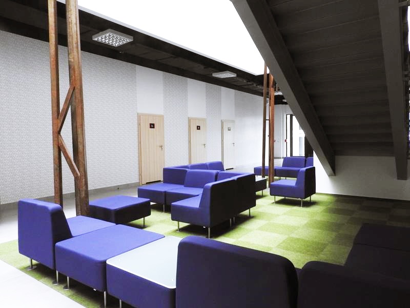 Nowoczesna strefa wypoczynkowa z niebieskimi i czarnymi meblami, drewnianymi belkami i jasnymi drzwiami.